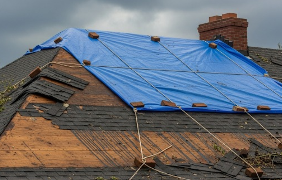 storm-damaged roof with missing shingles and a tarp secured for emergency stabilization