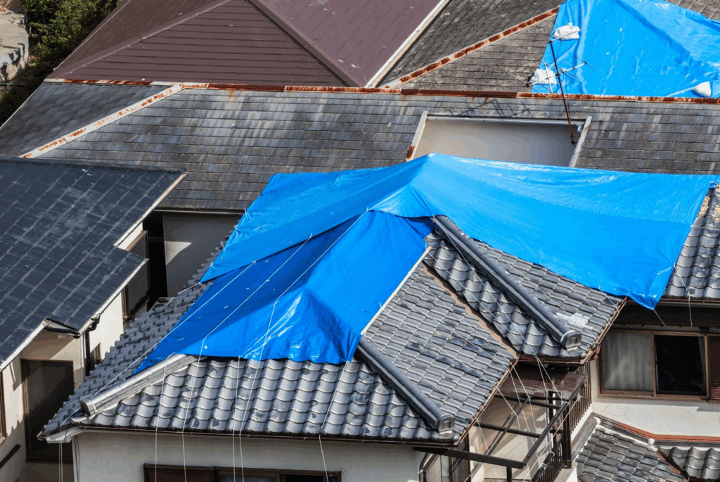 Houses with damaged tiled roof covered with blue tarp