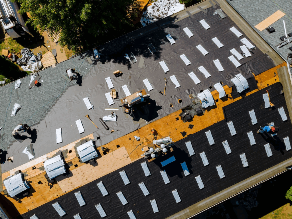 Workers replacing an old roof with new asphalt shingles during home roof construction and installation.