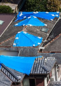Alt text: damaged roofs covered with blue tarp, signaling the need for roof leak repair near me